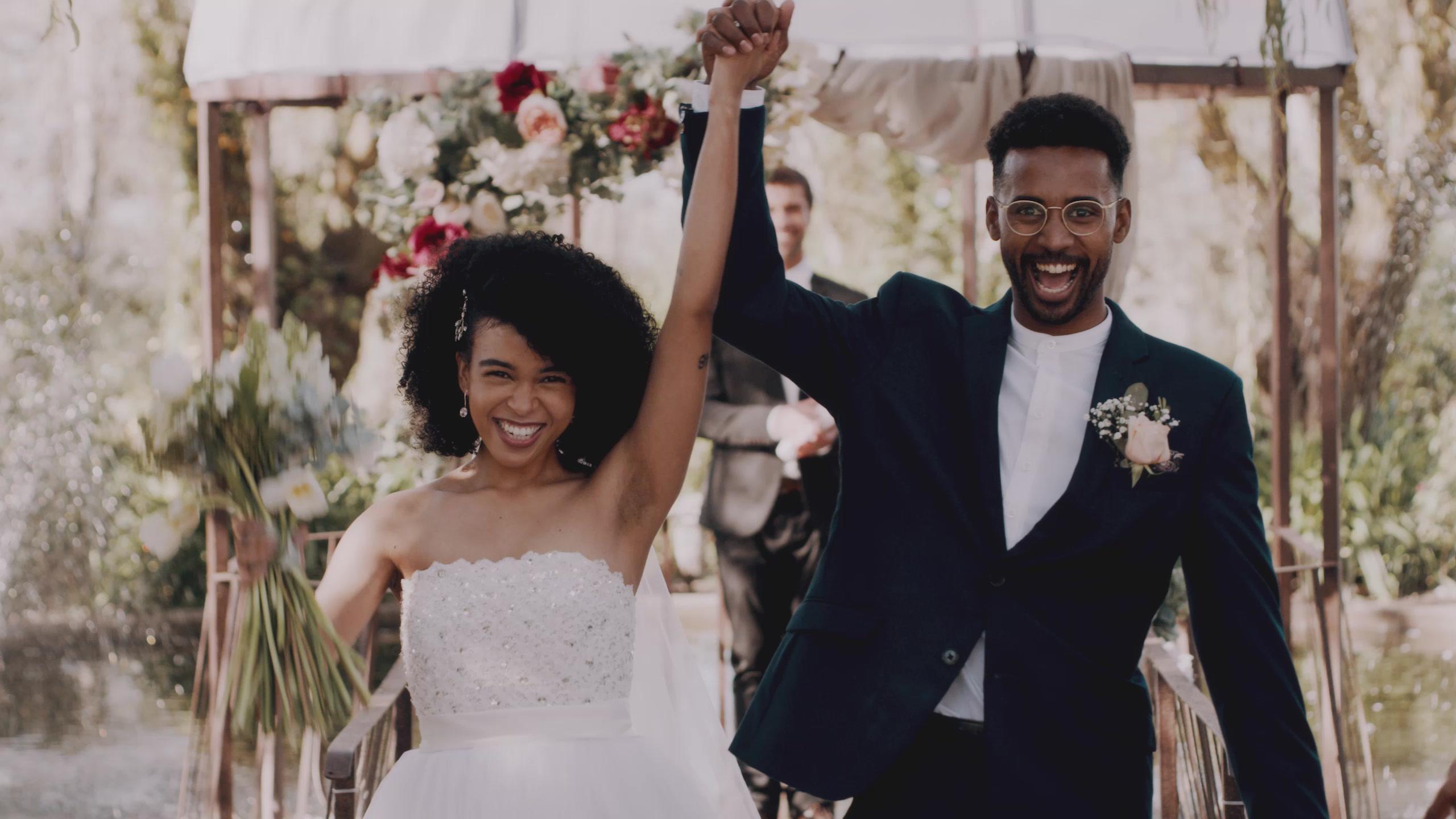 A newly married couple raising their hands after the ceremony, a floral arch behind them