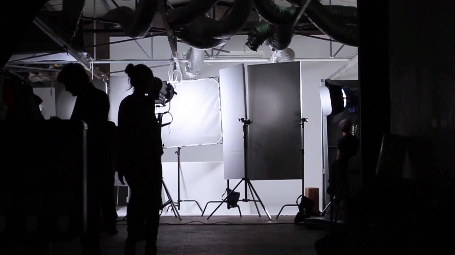 Two people in a photo studio in front of strobes, a reflector and light stands